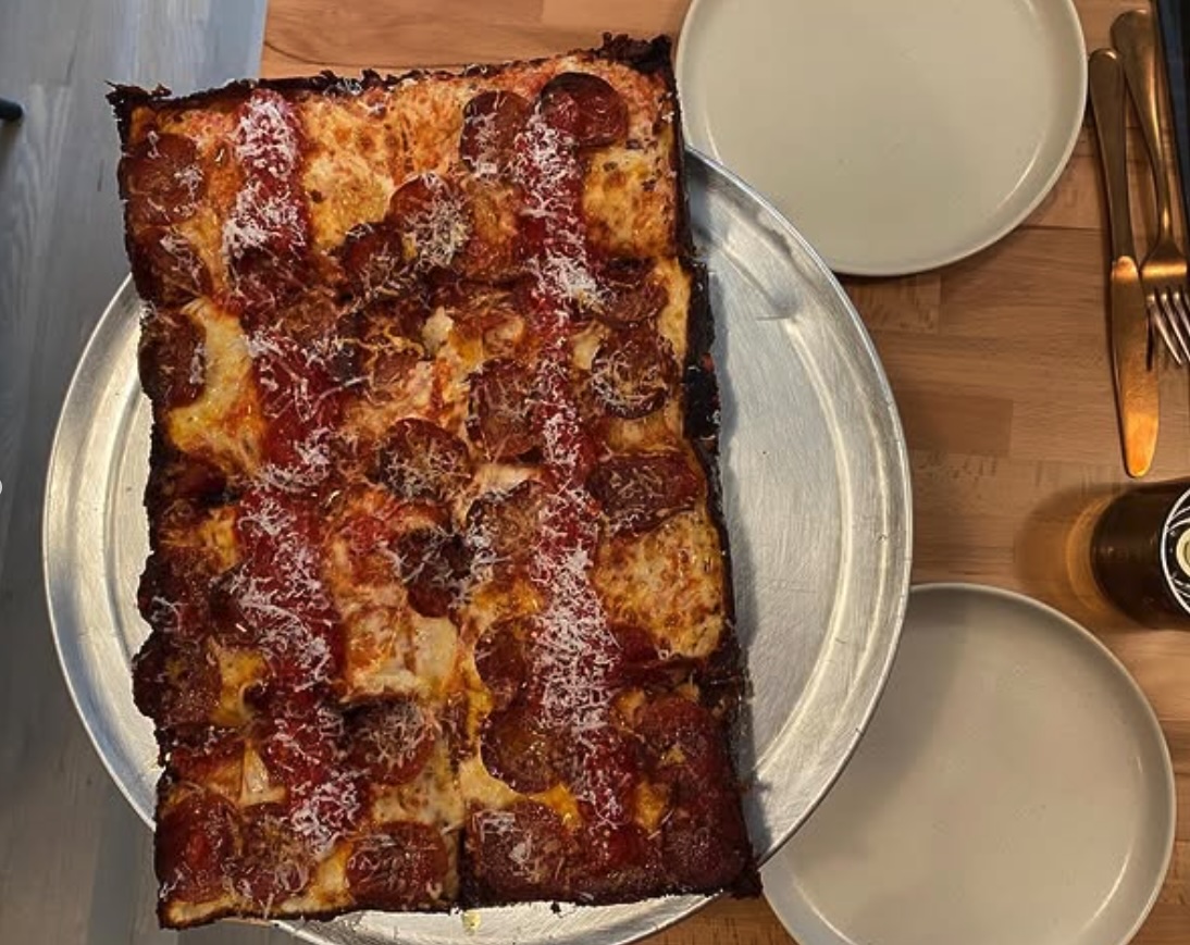 A rectangular Detroit style pizza with caramelized cheese edges, cut into squares