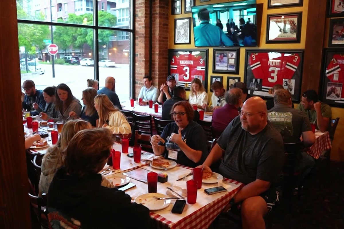 A visiting company team eating pizza together at a long table on a Chicago outing